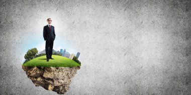 Yeşil yüzen adada beton zemine karşı duran kendine güvenen zarif iş adamı.