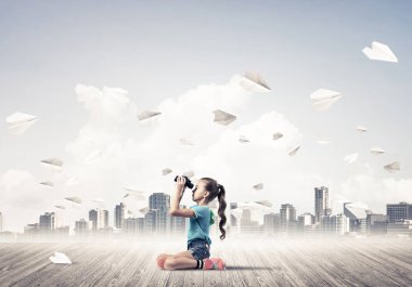 Ahşap zemin ve etrafında uçan kağıt uçaklar üzerinde oturan sevimli kız