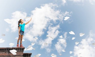 Binanın tepesinde kağıt uçakla oynayan sevimli, mutlu bir kız.