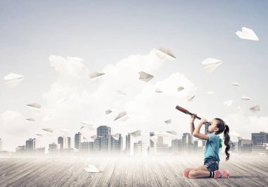 Ahşap zemin ve etrafında uçan kağıt uçaklar üzerinde oturan sevimli kız