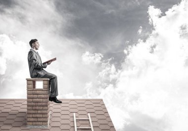 Elinde kırmızı kitap ile ev oturan takım elbiseli genç işadamı