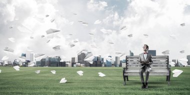 Kırmızı gözlüklü ve takım elbiseli komik adam bankta oturup kitap okuyor.