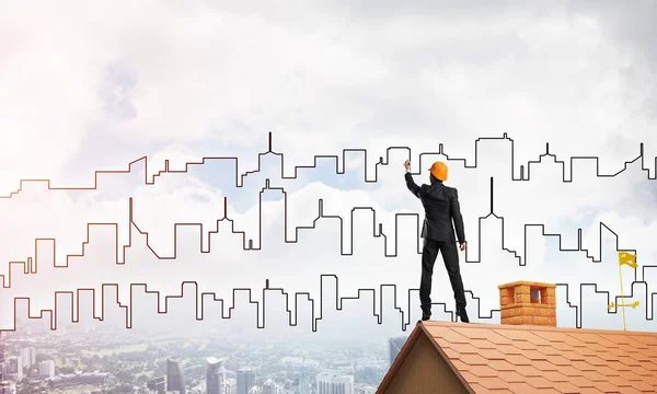 エンジニアの男が家の屋根の上に立って街を描く 混合メディア — ストック写真