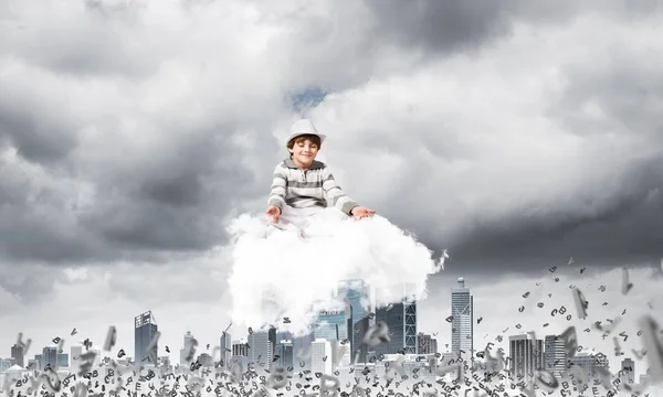都会の風景を背景に飛んでいる文字の間に雲の上に瞑想しながら目を閉じて集中して見ている若い男の子 — ストック写真