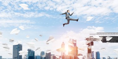 Kağıt uçaklar beton bridge uygulamasında zorlukların üstesinden sembolü olarak uçan ile gap üstünden atlayarak iş adamı. Cityscape zemin üzerine güneş ışığı ile. 3D render.