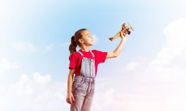 Elinde retro uçak modeliyle tulumlu şirin bir kız çocuğu.