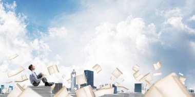 İş adamı uzak belgeler arasında kitap Clear sky ile arka plan üzerinde uçan yığını üzerinde otururken arıyorum. Karışık teknik.