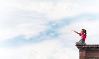 Üstte oturan ve bir şeyi işaret eden sevimli bir kız.