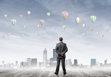 Arka ayakta ve havada uçan aerostats bakarak bir işadamı