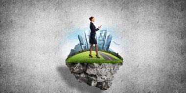 Yeşil yüzen adada beton zemine karşı duran kendine güvenen zarif bir iş kadını.