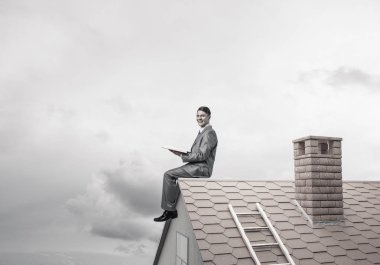 Elinde kırmızı kitap ile ev oturan takım elbiseli genç işadamı