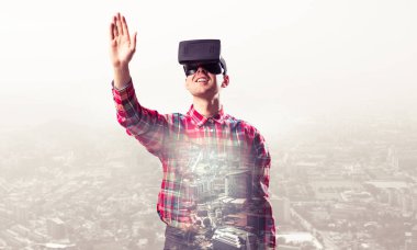 Sanal gerçeklik kulaklığı olan genç bir adam ya da şehrin arka planında 3 boyutlu gözlüklü.