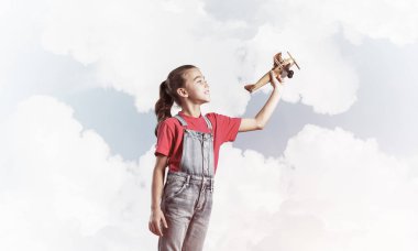 Elinde retro uçak modeliyle tulumlu şirin bir kız çocuğu.