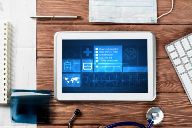 Beyaz tablet bilgisayar ve doktor aletleri ahşap masada.