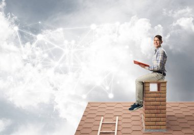 Elinde kırmızı kitap ile evin baca üzerinde oturan genç öğrenci adam