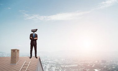 Evin çatısında baş durmak yerine kamerayla zum yapan yüzü olmayan bir iş adamı.