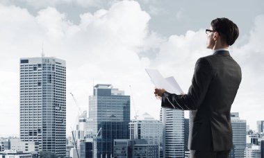 Elinde kağıtları olan genç ve zarif bir işadamı başka tarafa bakıyor.