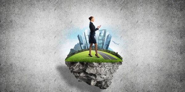 Yeşil yüzen adada beton zemine karşı duran kendine güvenen zarif bir iş kadını.