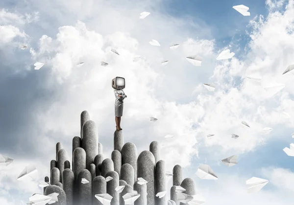 Business woman in suit with an old TV instead of head keeping arms crossed while standing on the top of stone columns among flying paper planes with beautiful landscape on background. 3D rendering.