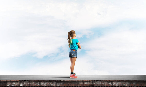 Cute kid girl standing on building roof with hands crossed on chest