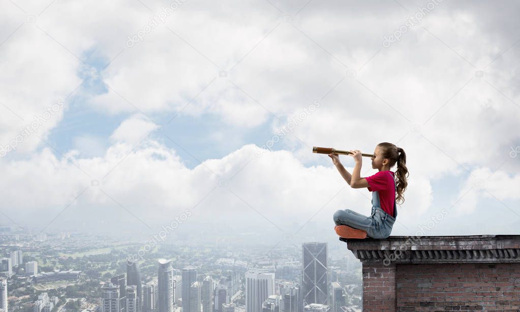 Cute kid girl sitting on house roof and looking in spyglass