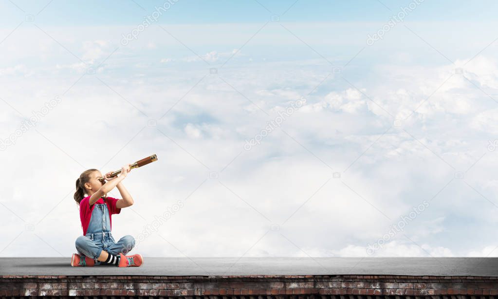 Cute kid girl sitting on house roof and looking in spyglass