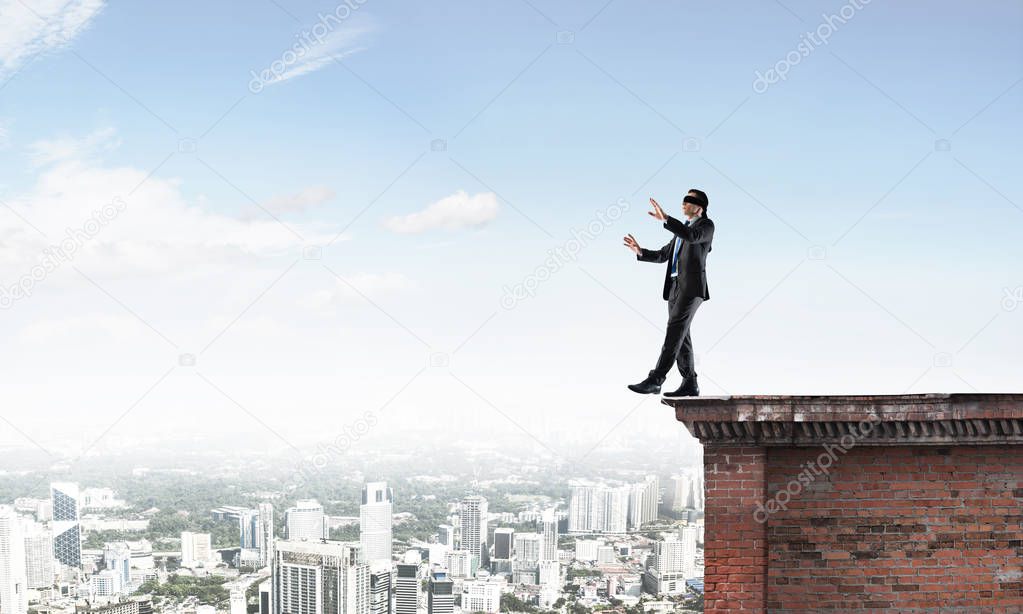 Businessman with blindfolder on eyes walking on building top