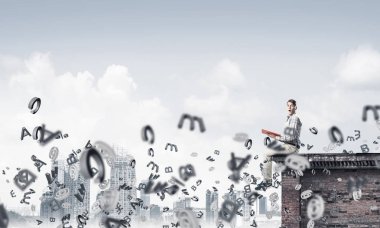 Elinde kırmızı kitap ile üst yapı üzerinde rahat oturan genç adam