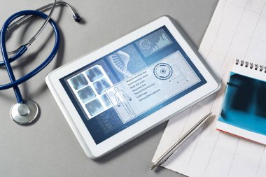 Gri yüzeyde beyaz tablet ve doktor araçları