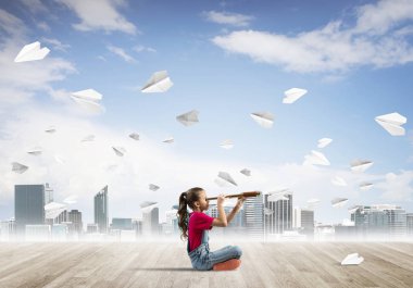 Ahşap zemin ve etrafında uçan kağıt uçaklar üzerinde oturan sevimli kız