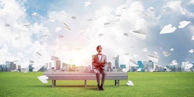 Kırmızı gözlüklü ve takım elbiseli komik adam bankta oturup kitap okuyor.