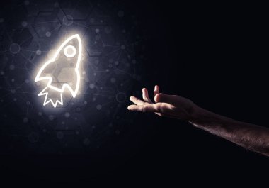 Koyu arkaplanda parlayan roket simgesi ve insan eli