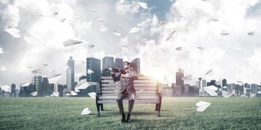 Takım elbiseli ve gözlüklü genç adam bankta oturup keman çalıyor.