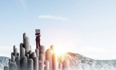 Arka plan üzerinde duran güzel gökyüzü ile taş sütun üst dizüstü bilgisayar kafasına silah tutmak yerine ile takım elbiseli işadamı geçti.