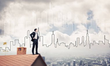 Kararlı genç işadamı evin çatısında dikiliyor ve başka tarafa bakıyor. Karışık ortam