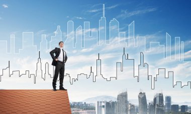 Kararlı genç işadamı evin çatısında dikiliyor ve başka tarafa bakıyor. Karışık ortam