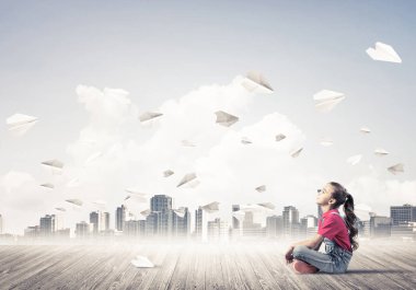 Ahşap zemin ve etrafında uçan kağıt uçaklar üzerinde oturan sevimli kız