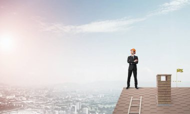 Takım elbiseli genç işadamı ve çatıda kask var. Karışık ortam