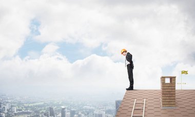 Genç işadamı tuğladan çatının kenarında dikilip aşağıya bakıyor. Karışık ortam