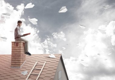 Elinde kırmızı kitap ile ev üzerinde oturan genç adam