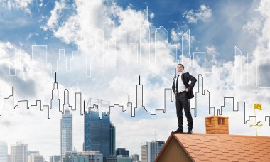 Kararlı genç işadamı evin çatısında dikiliyor ve başka tarafa bakıyor. Karışık ortam