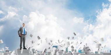 Kendine güvenen işadamı belgeleri kağıtları Clear sky ile arka plan üzerinde uçan arasında yığını üzerinde takım elbise ayakta. Karışık teknik.