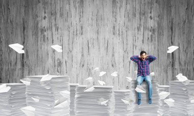 Arka plan gri duvar ile kağıt uçan arasında casual giyim oturan genç adam uçakları. Karışık teknik.