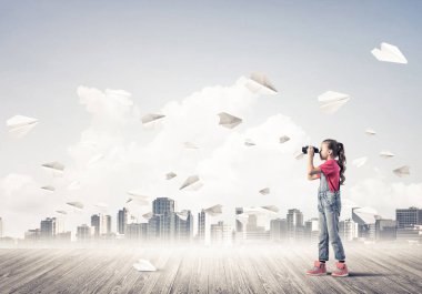 Şirin kız tahta zeminde durur ve kağıt uçaklar uçuşur.