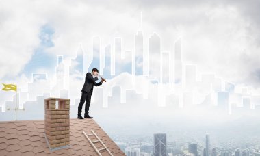 Çatıda takım elbiseli genç bir işadamı var. Karışık ortam