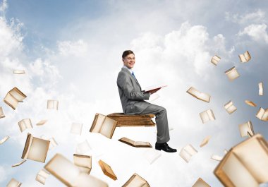 Genç işadamı ellerinde kırmızı kitap ile mavi gökyüzünde yüzen