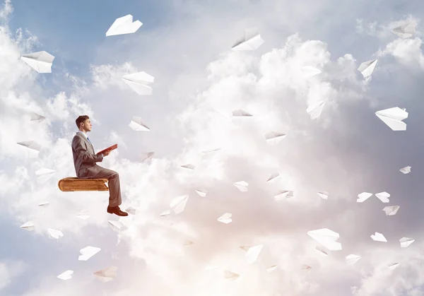 年轻的生意人坐在漂浮在空气中的书与一个在手 — 图库照片
