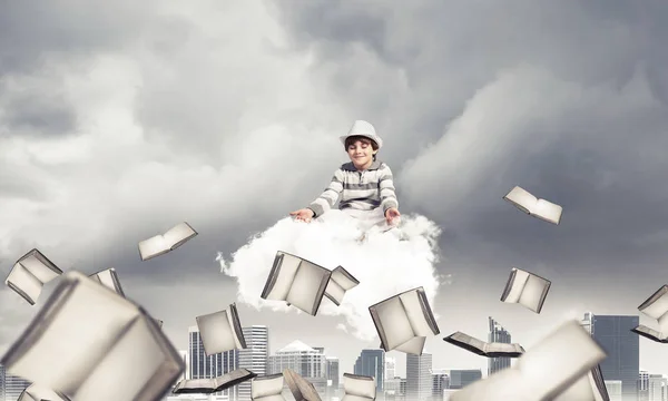 都会の景色を背景に本を飛んでいる間に雲の上で瞑想しながら目を閉じて集中して見ている若い男の子 — ストック写真
