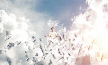 Beyaz elbiseli adam gözlerini kapalı tutuyor ve odaklanmış görünüyor. Aynı zamanda havada uçan kağıtların arasında meditasyon yapıyor. Arka planda bulutlu bir gökyüzü var..
