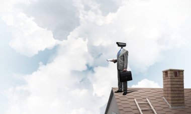 Evin çatısında baş durmak yerine kamerayla zum yapan yüzü olmayan bir iş adamı.